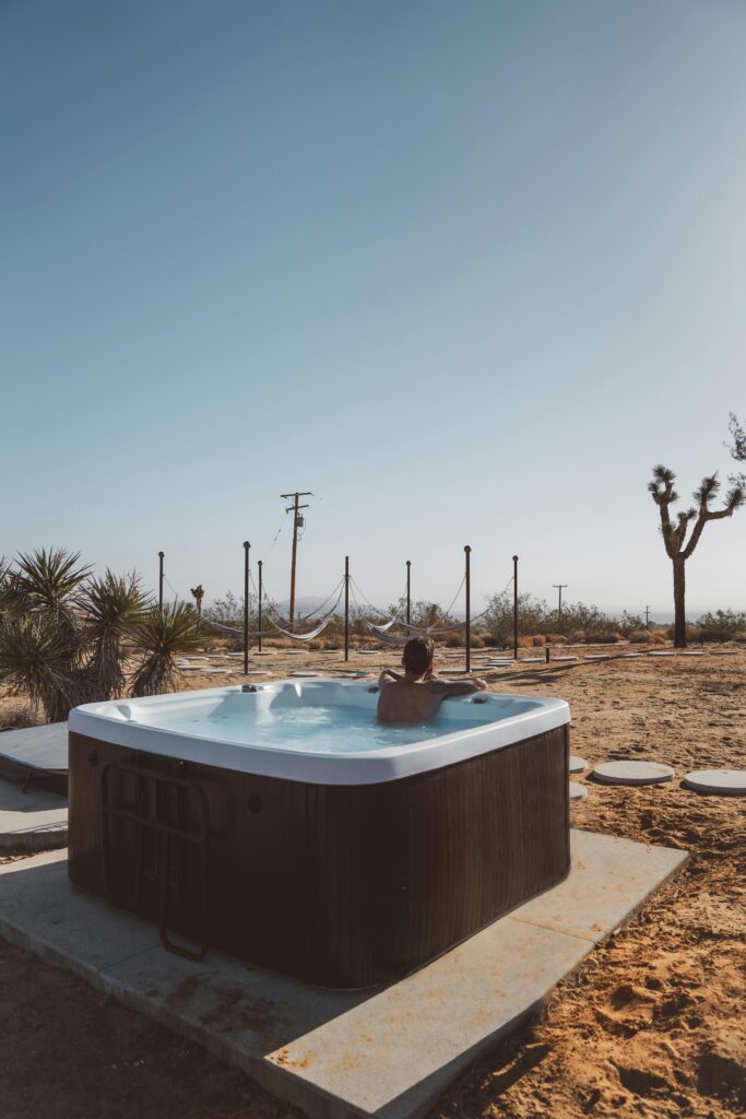 Man enjoying a hot tub in the serene landscape of Joshua Tree desert under a clear blue sky.